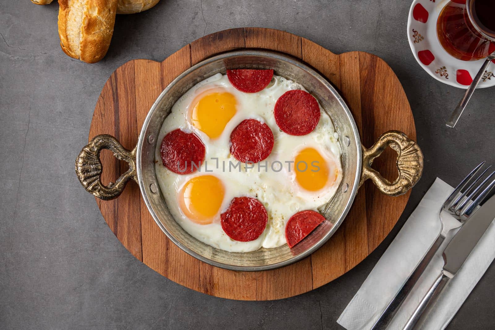 fried eggs with turkish sausage with bread and tea on dark stone table by Sonat