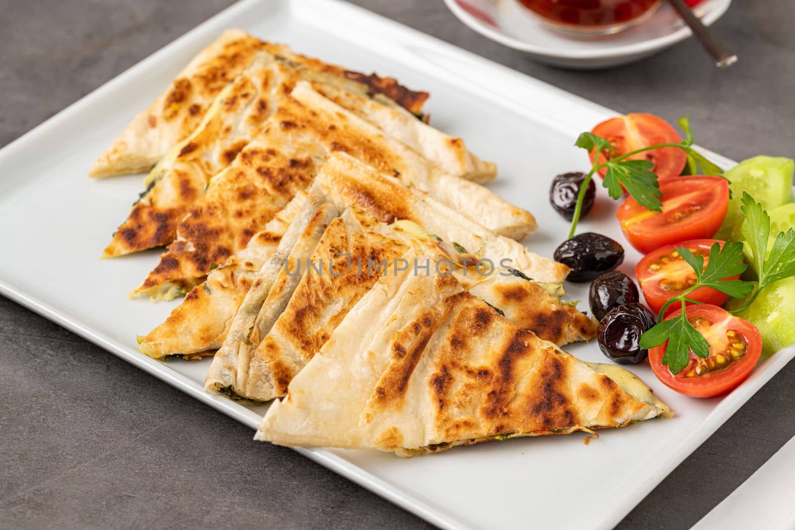 Traditional Turkish flatbread or Gozleme with tomatoes, olives and tea on dark stone table