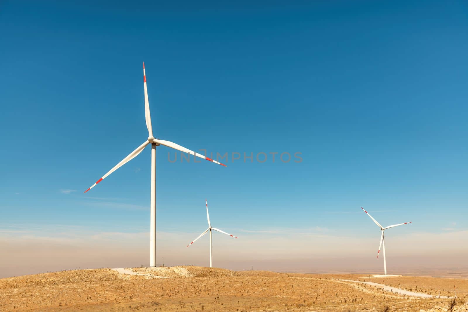 Multiple wind turbines standing on a hill at sunset and generating electricity