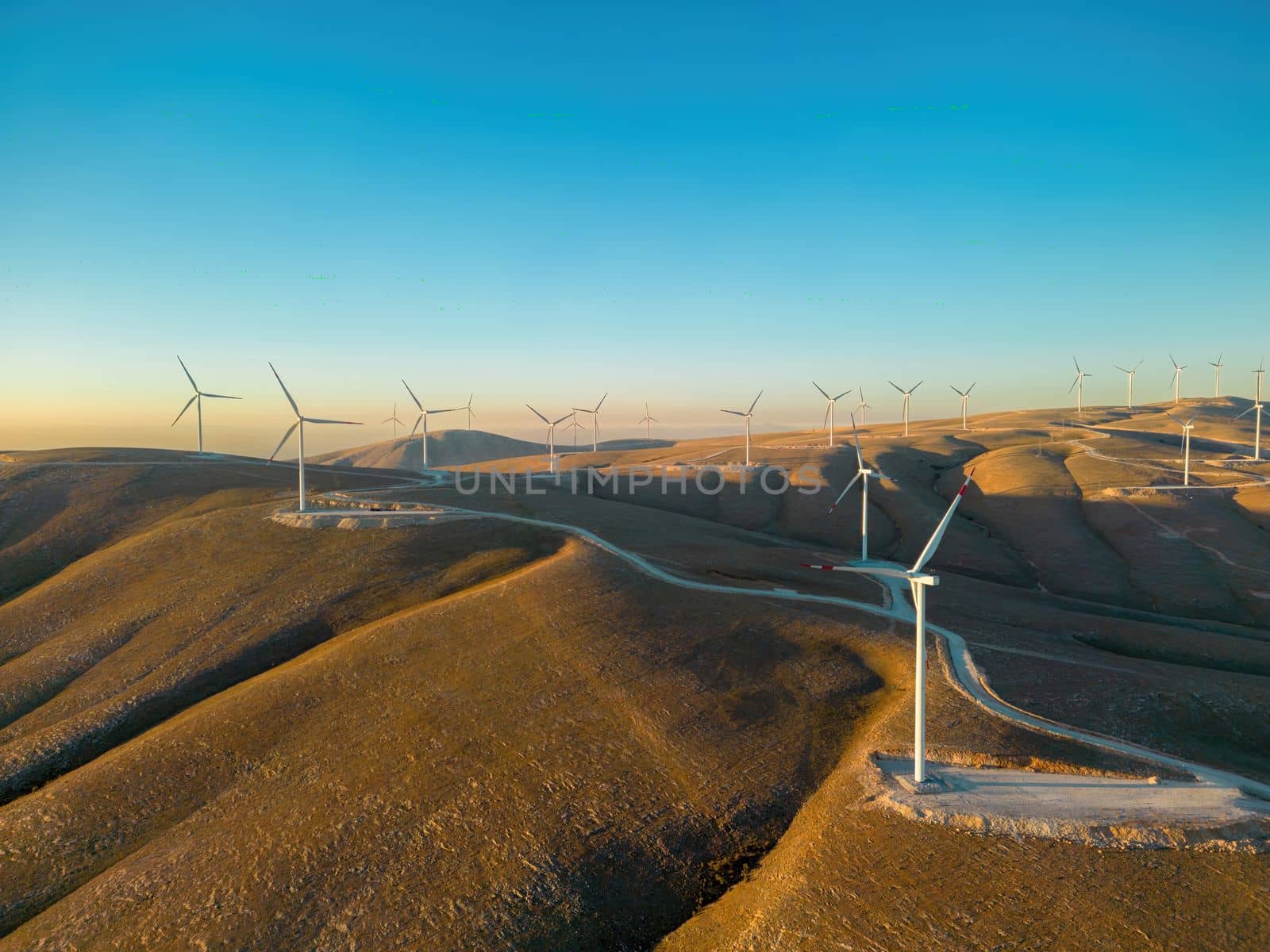 Aerial view of multiple wind turbines standing on a hill and generating electricity at sunrise