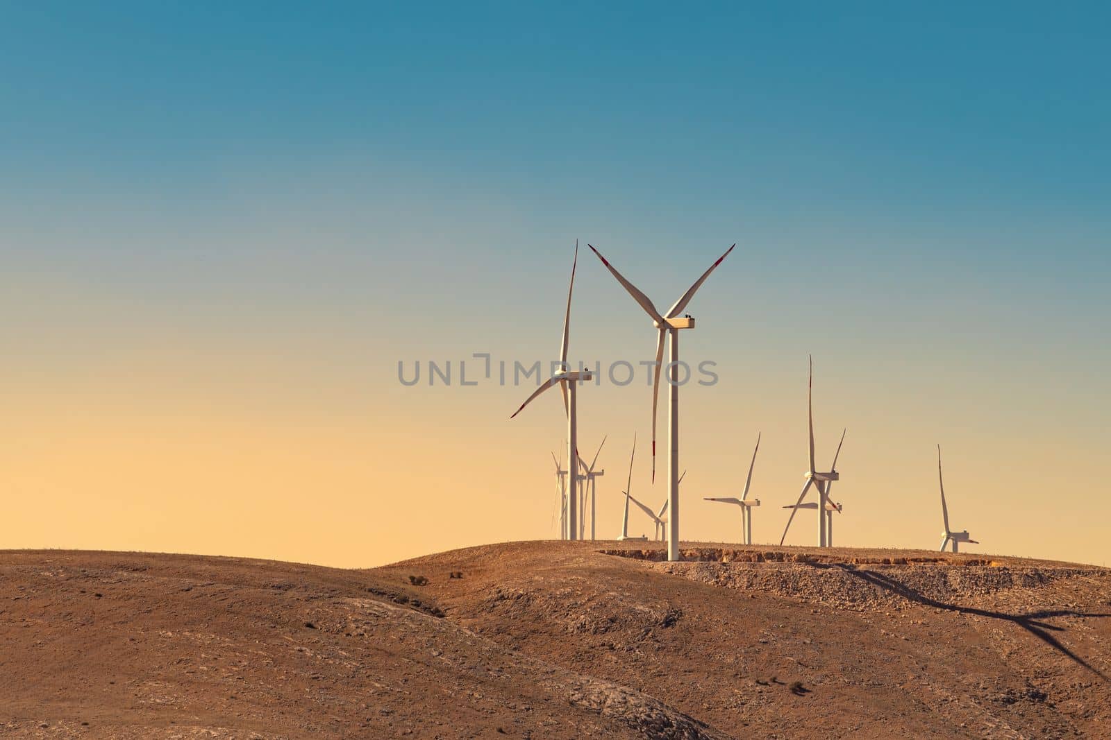 Multiple wind turbines standing on a hill at sunset and generating electricity