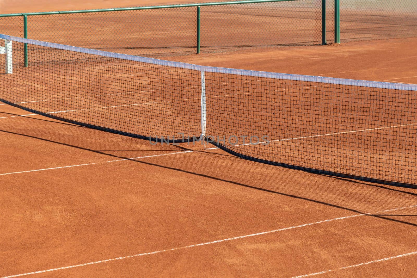 Baseline and net of an empty clay tennis court on a sunny day by Sonat