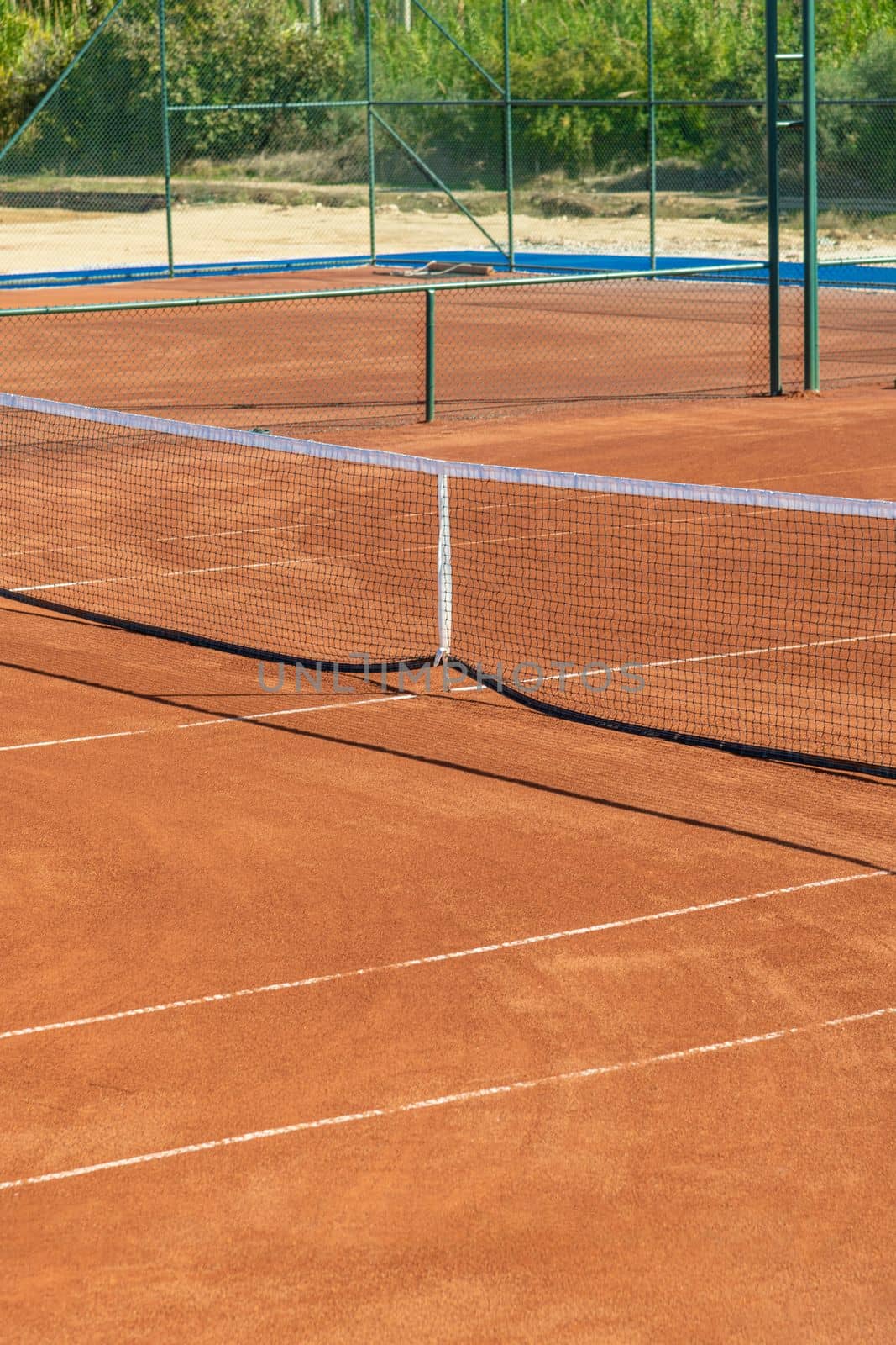 Baseline and net of an empty clay tennis court on a sunny day by Sonat