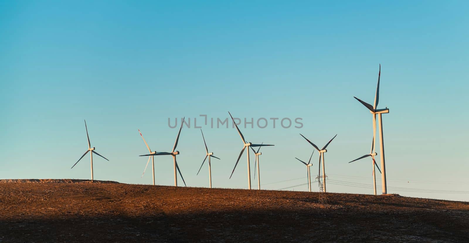 Multiple wind turbines standing on a hill at sunrise and generating electricity