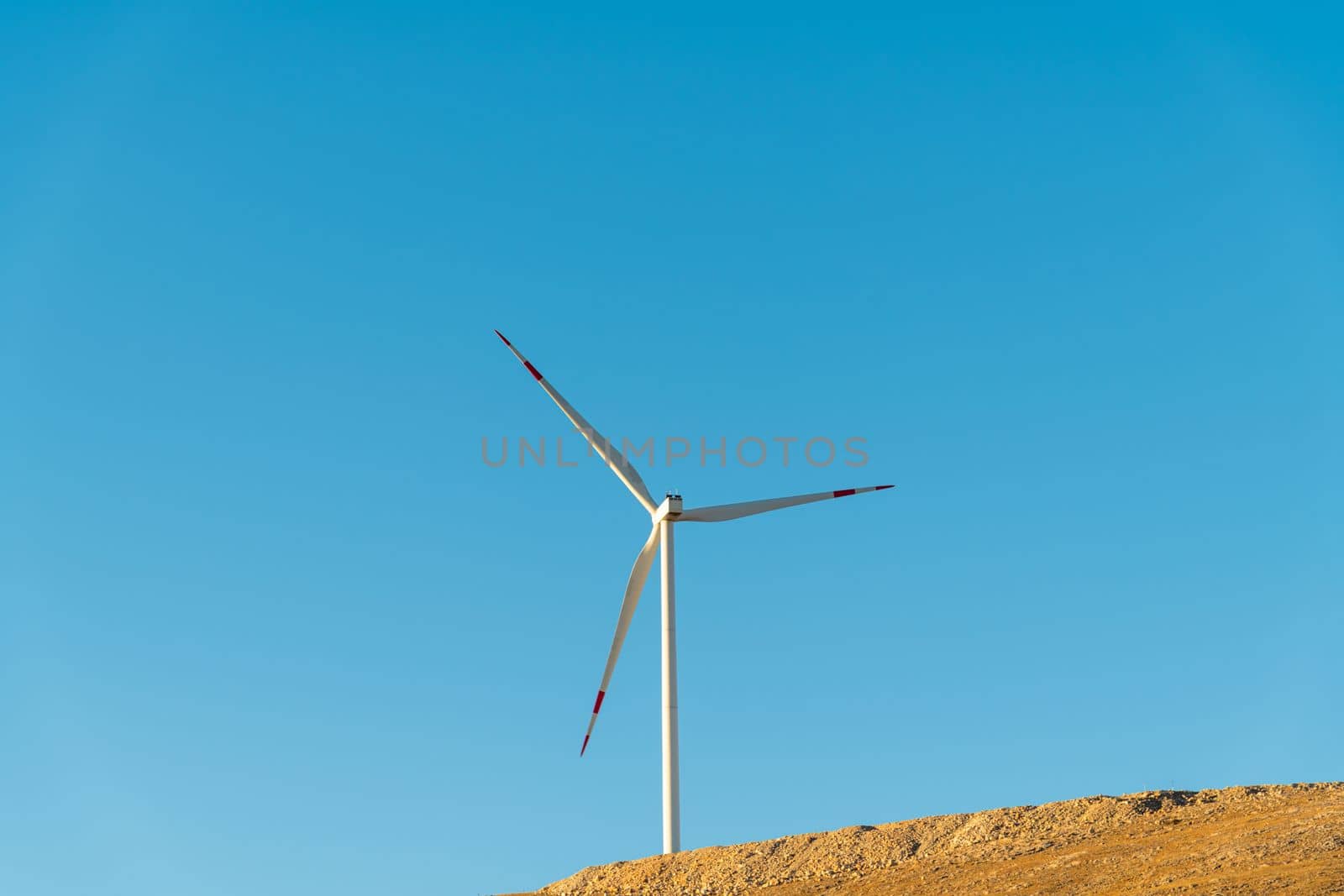 Wind turbine standing on a hill and generating electricity at sunrise