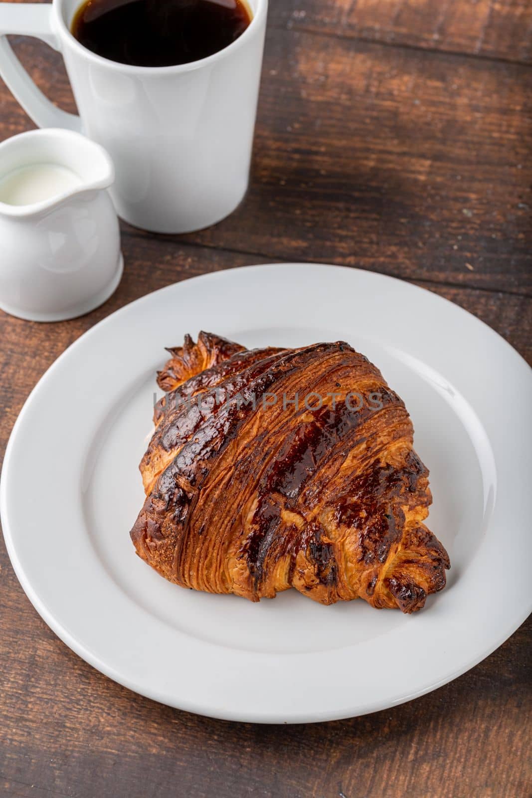 Croissant with coffee next to it on wooden table by Sonat