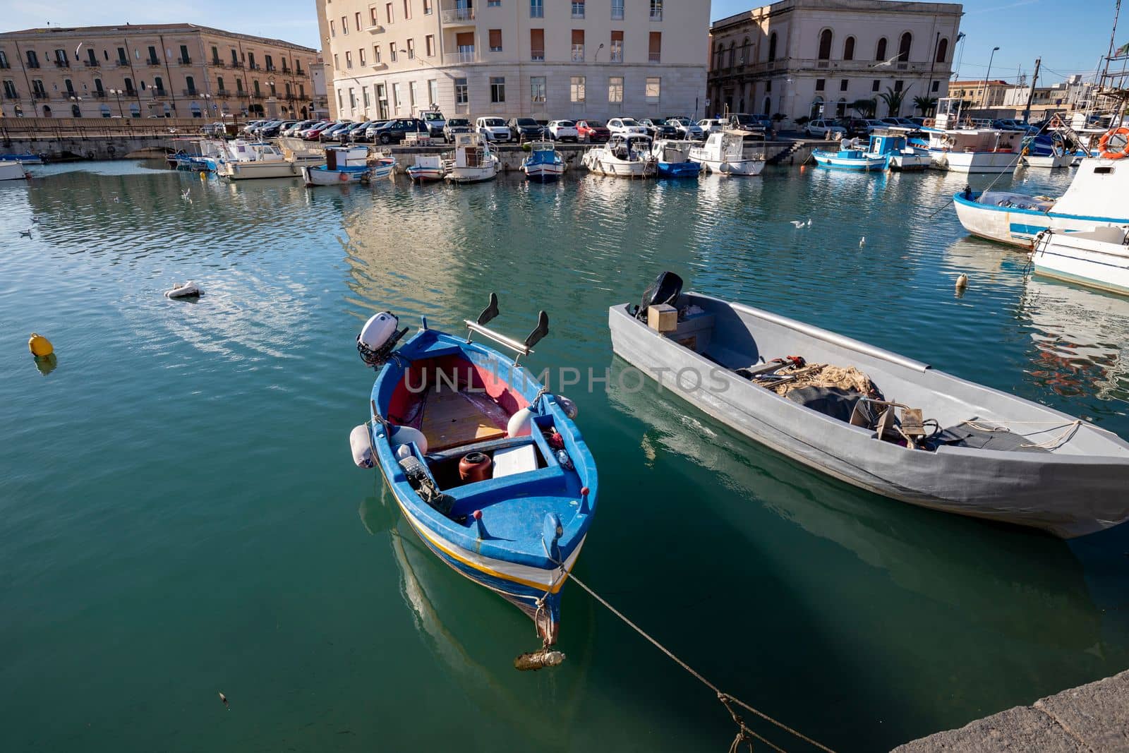 Fishing boats on the water in Ortigia island with the cityscape of Syracuse in Sicily, Italy