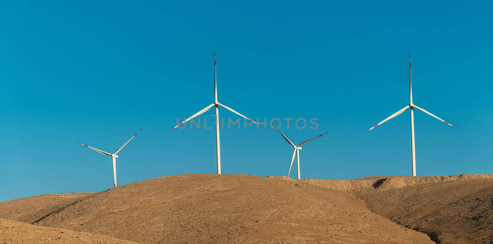 Multiple wind turbines standing on a hill at sunrise and generating electricity