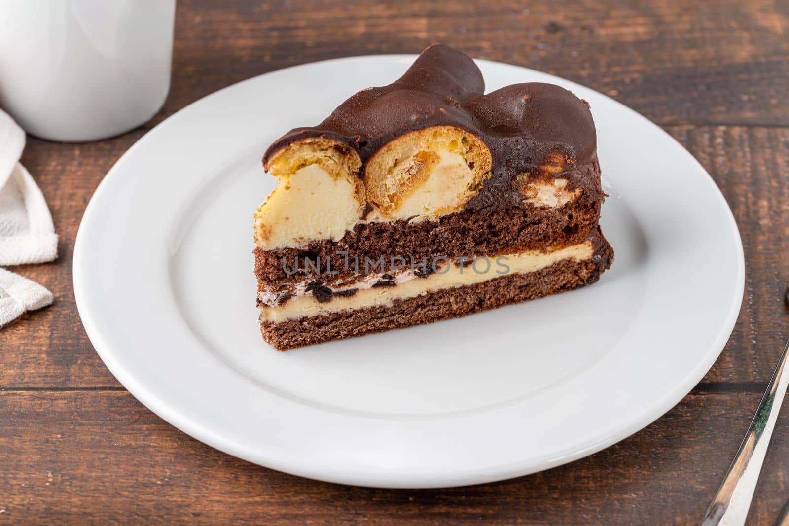 Cake with profiteroles on a white porcelain plate with filter coffee on the side by Sonat