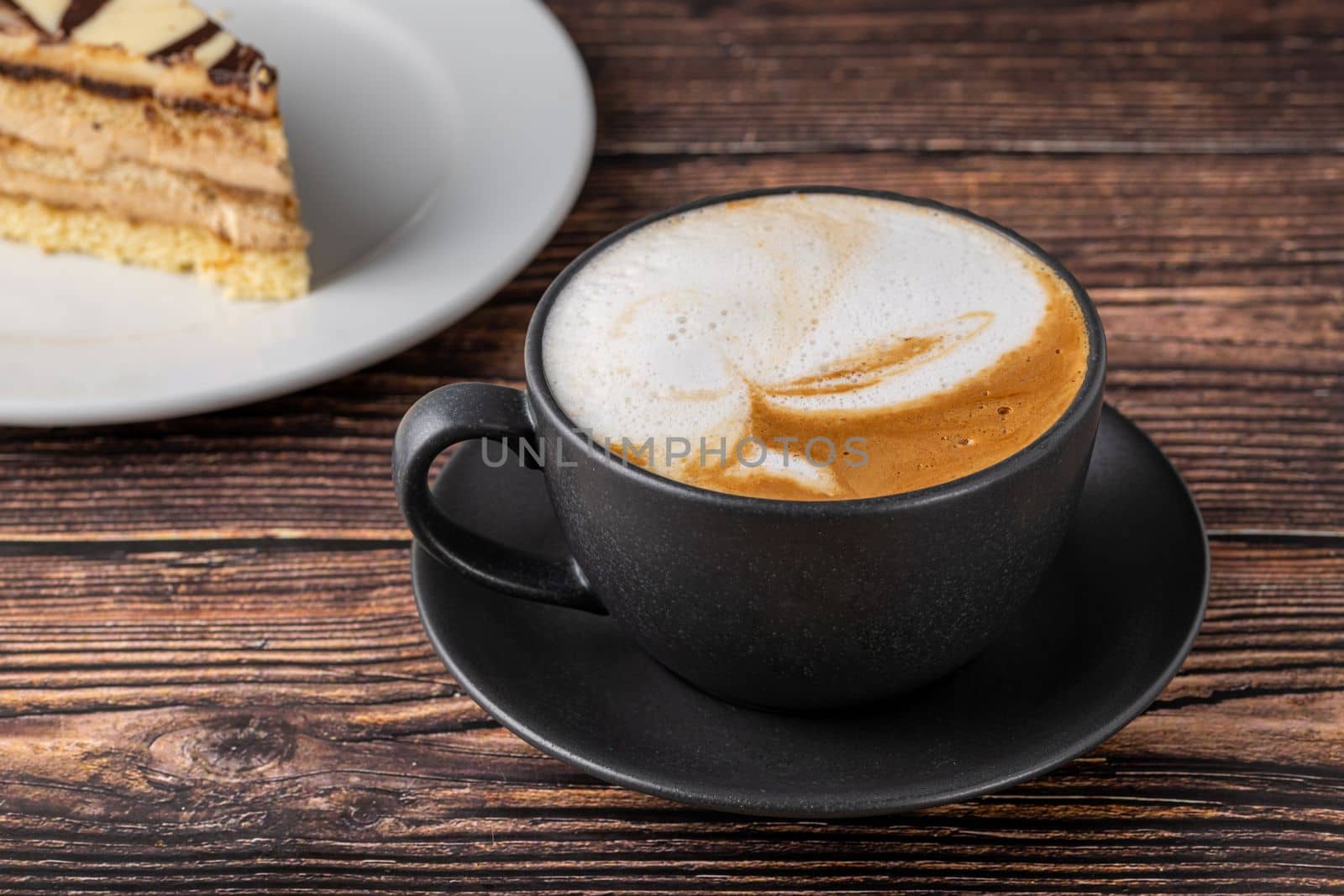 Relaxing latte coffee in black porcelain cup on wooden table