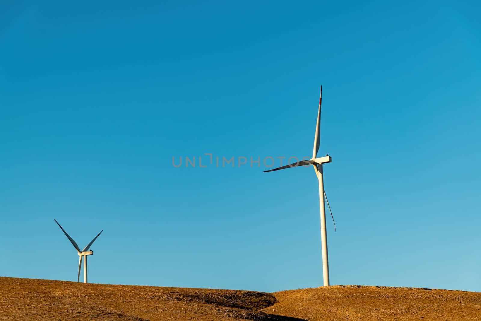 Multiple wind turbines standing on a hill at sunrise and generating electricity