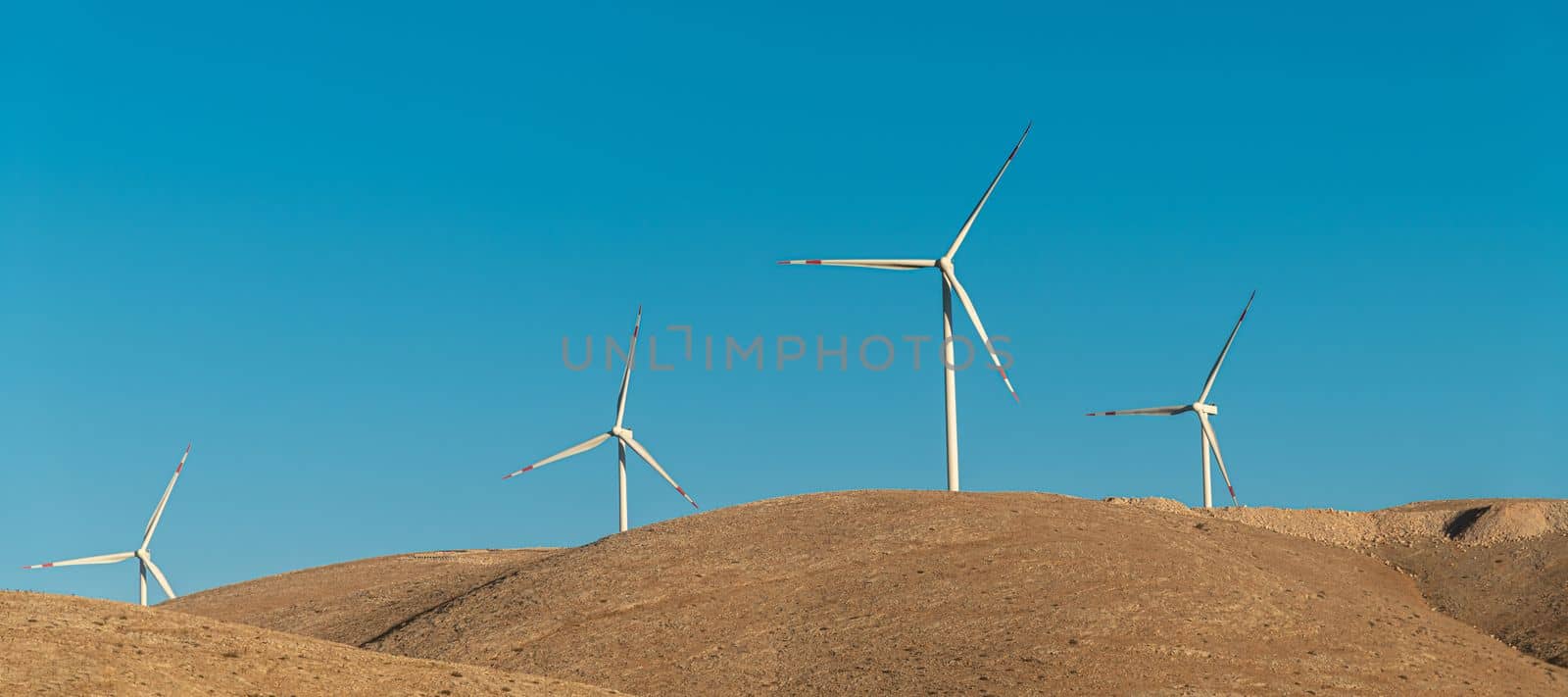 Multiple wind turbines standing on a hill at sunrise and generating electricity by Sonat