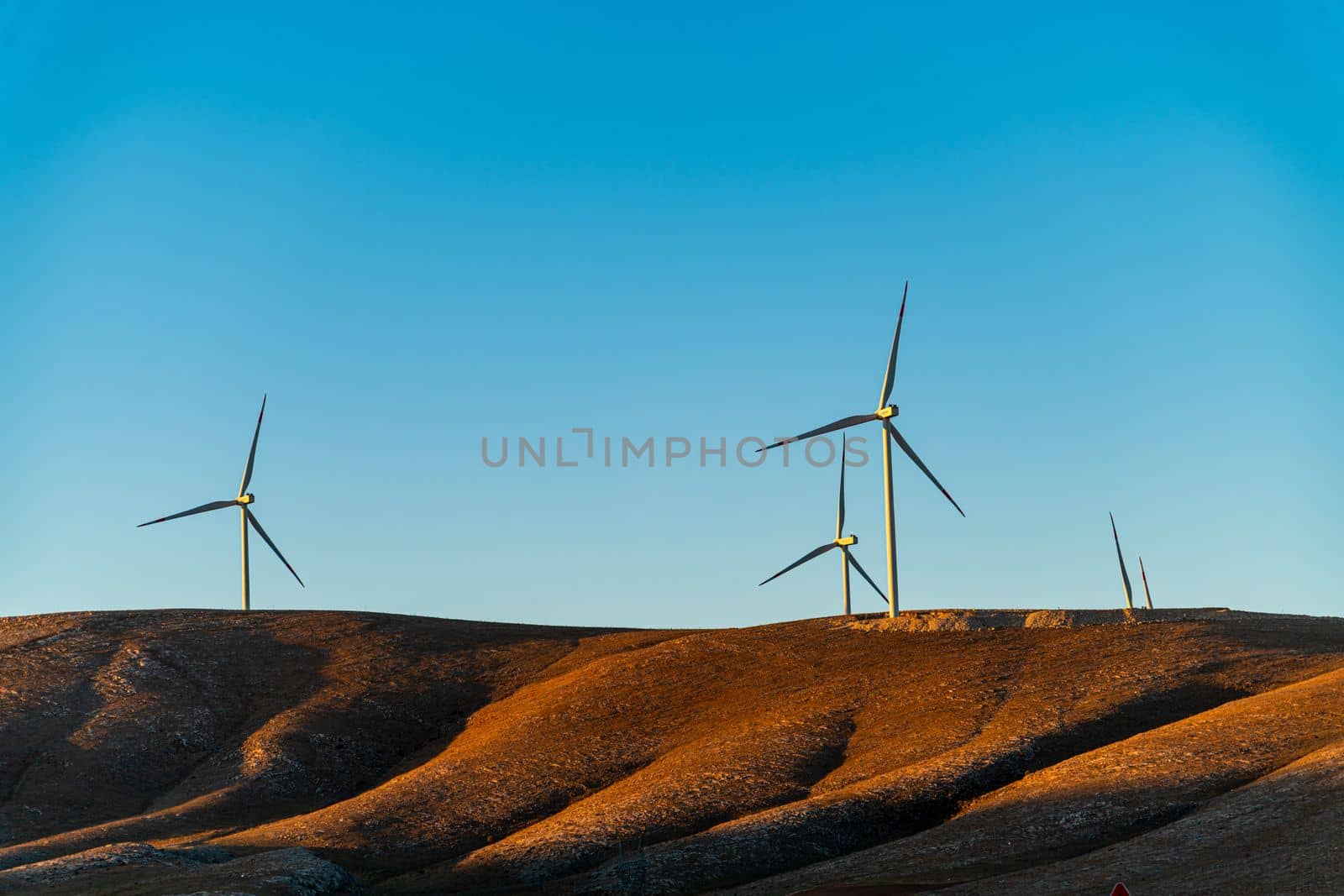 Multiple wind turbines standing on a hill at sunrise and generating electricity