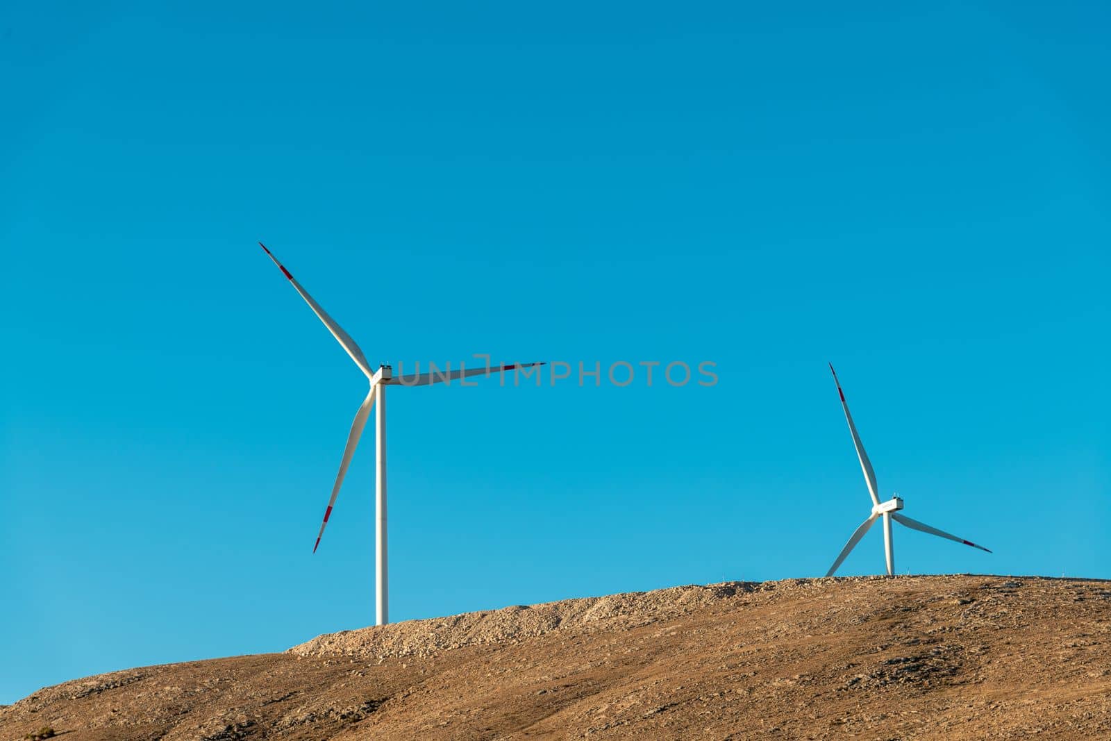 Multiple wind turbines standing on a hill at sunrise and generating electricity