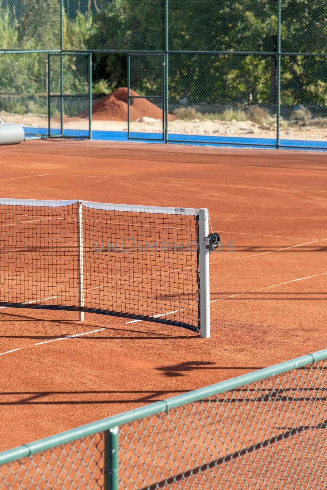 Baseline and net of an empty clay tennis court on a sunny day by Sonat