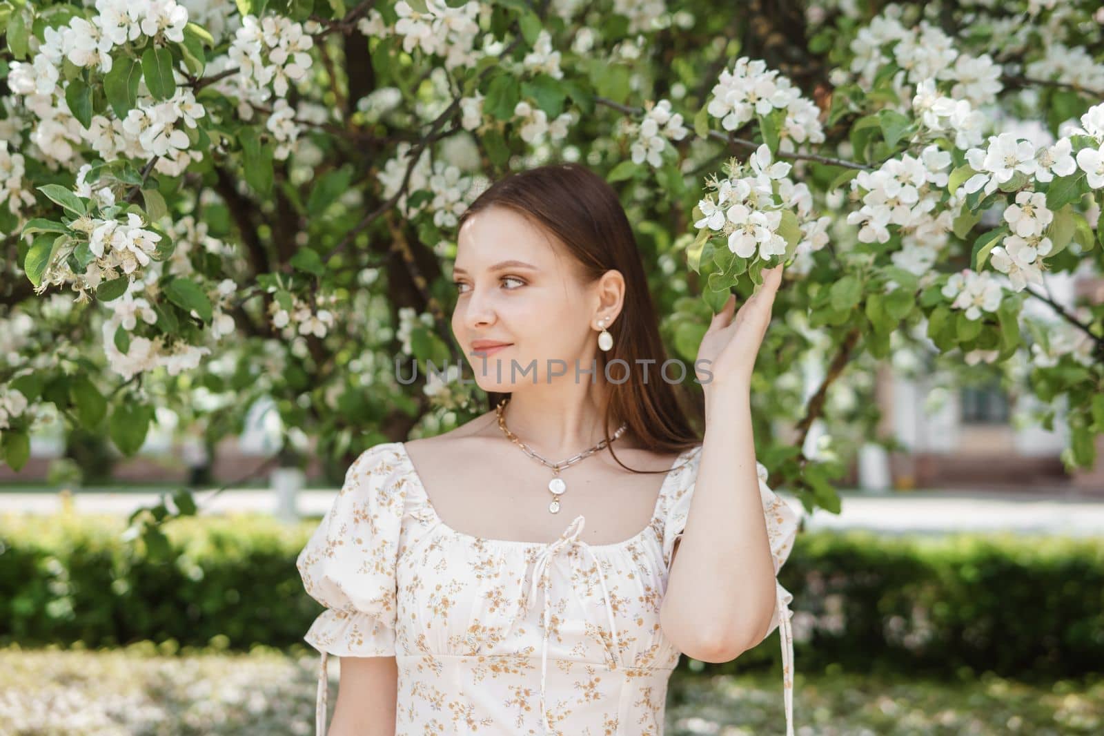 An attractive long-haired woman walks in the spring in the park of blooming apple trees. Spring portrait of a woman