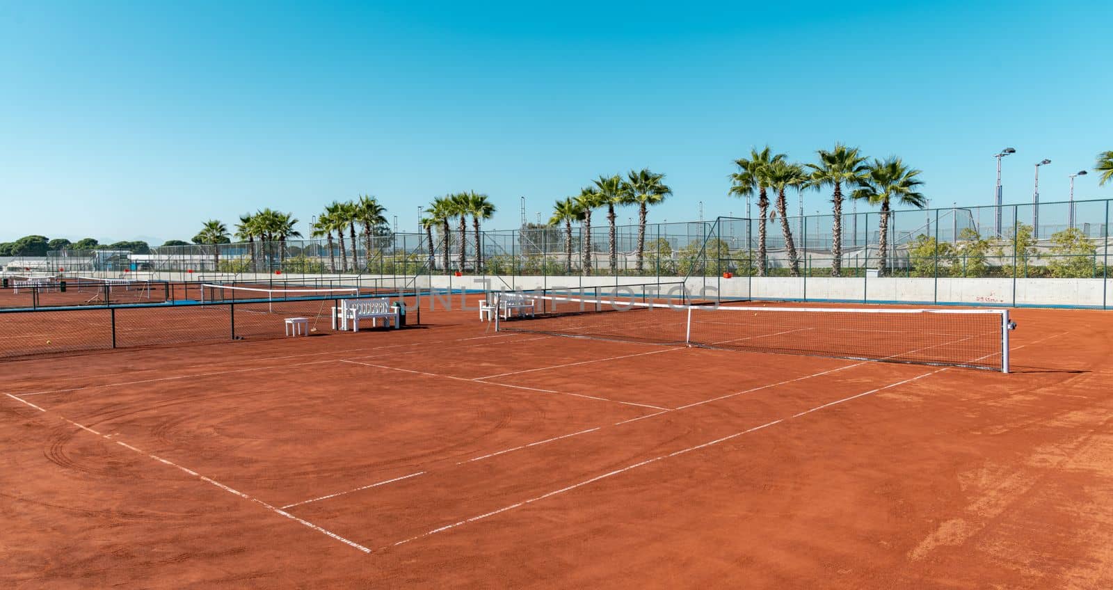 Baseline and net of an empty clay tennis court on a sunny day