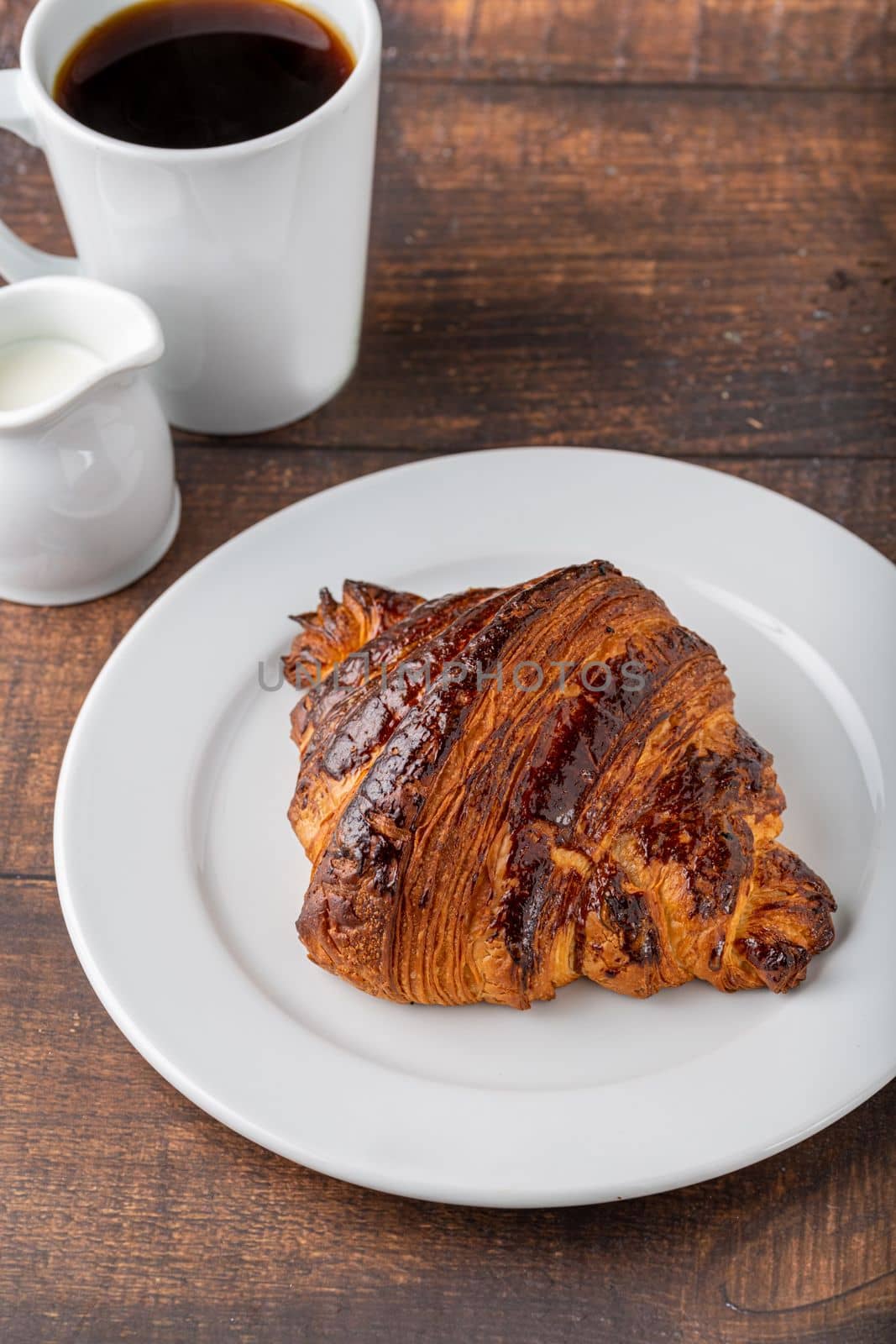 Croissant with coffee next to it on wooden table