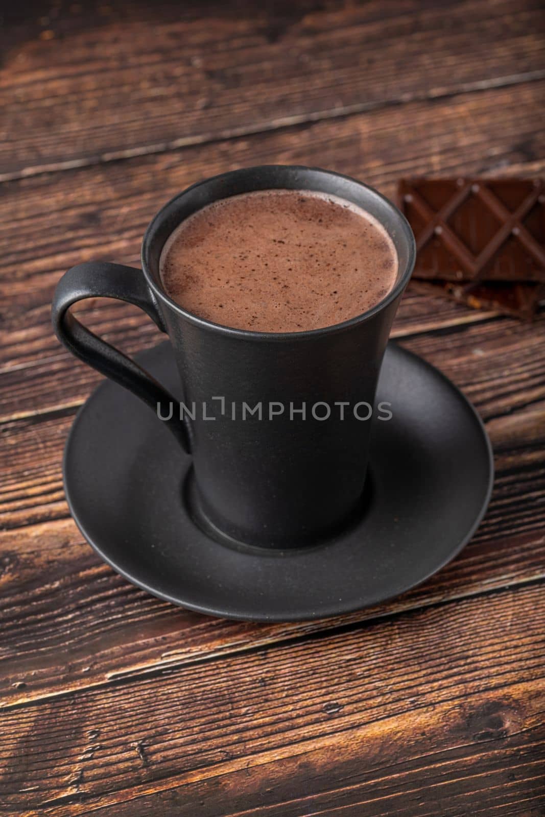 Hot chocolate in a black porcelain cup with a chocolate bar next to it