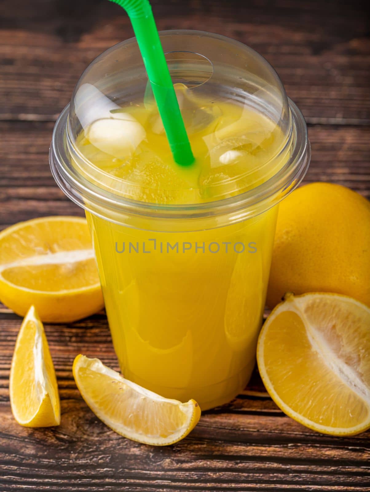 Lemonade in a take away glass with cut lemon next to it on wooden table by Sonat