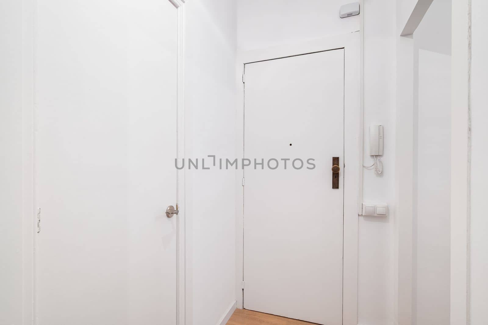 White front door to apartment with intercom on wall. There is peephole in door for observing what is happening outside. Door lock protects the apartment from the entry of unauthorized persons.