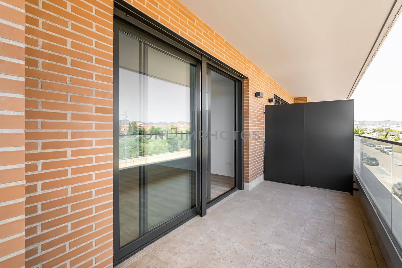 Large entrance balcony door made of black plastic with a sliding system. Terrace with marble floor and glass railings. The walls of the building are made of yellow bricks. by apavlin