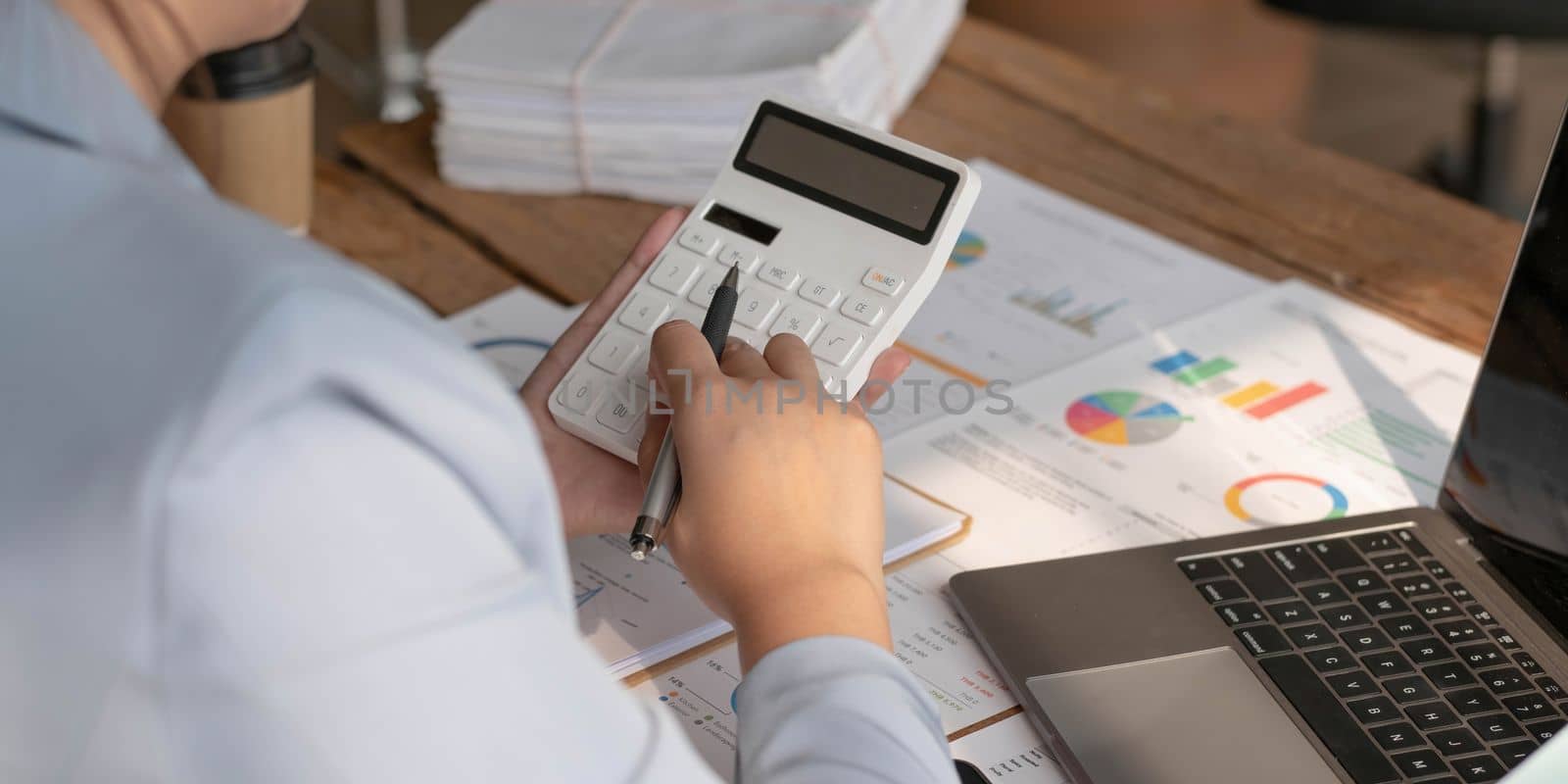Business woman using calculator to calculate financial report, working at office with laptop computer on table. Asian female accountant or banker making calculations. finances and economy concept by wichayada