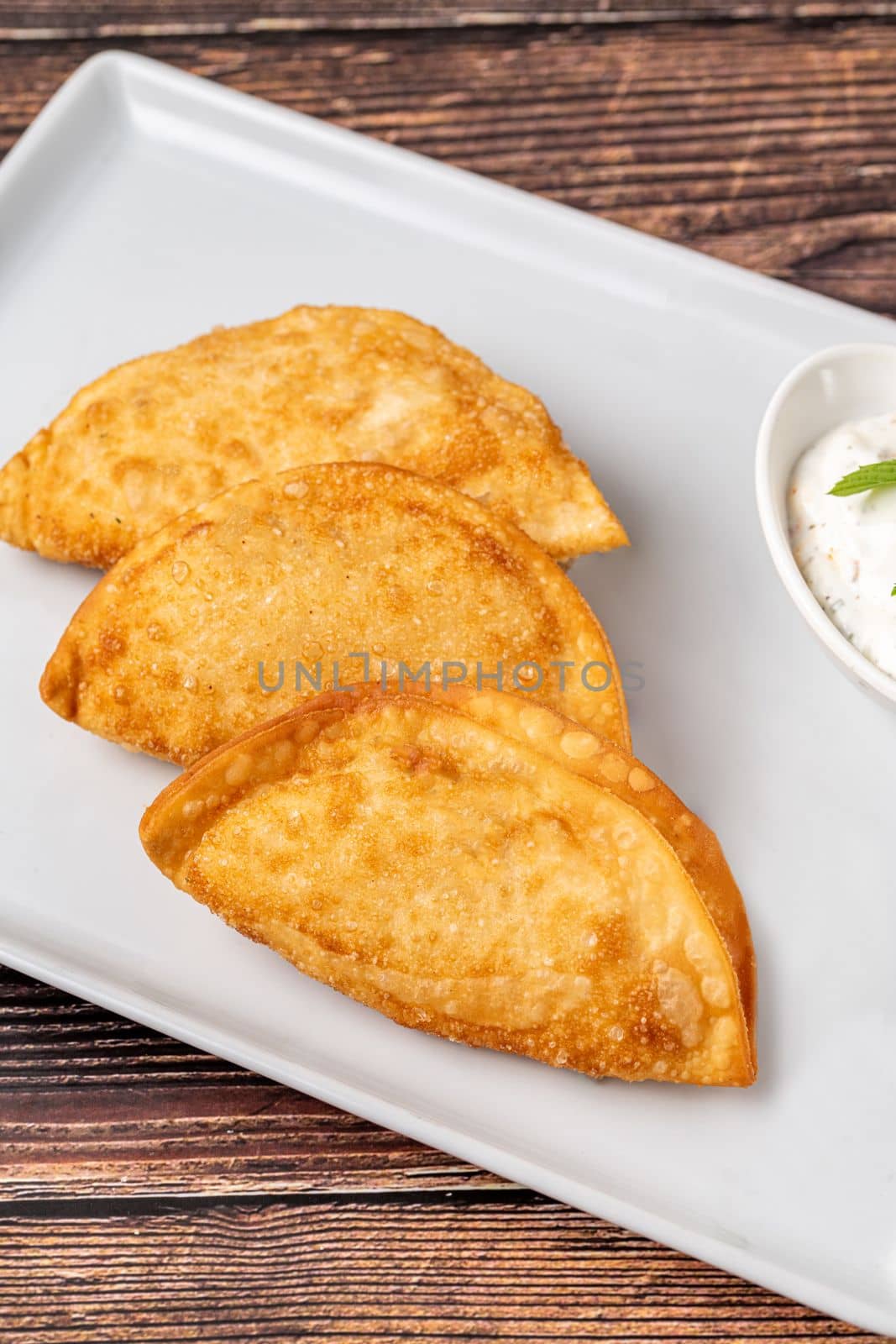 Beef Cheburek on a wooden table. Deep Fried Beef Dumplings with meat and onions. Turkish name Ci Borek or Cig Borek by Sonat