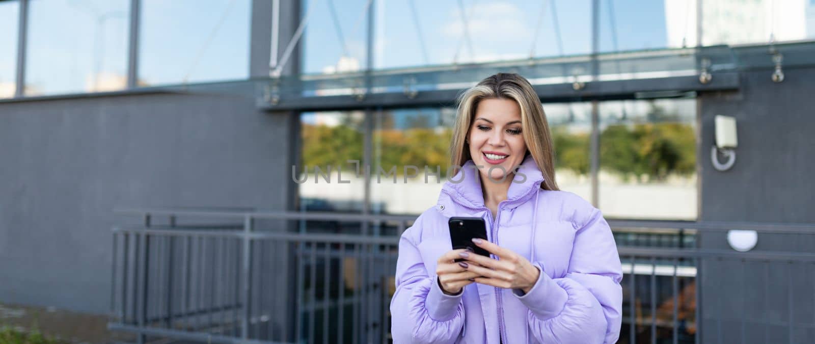 adult caucasian woman looking at phone screen outside with smile.