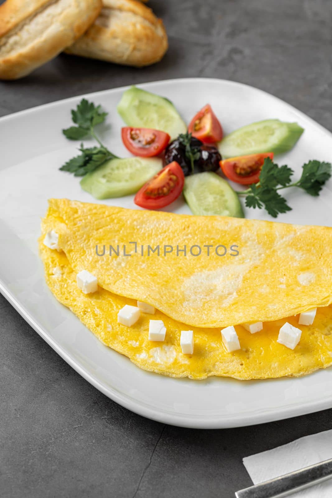 Feta cheese omelet with olives and tomatoes on a white porcelain plate