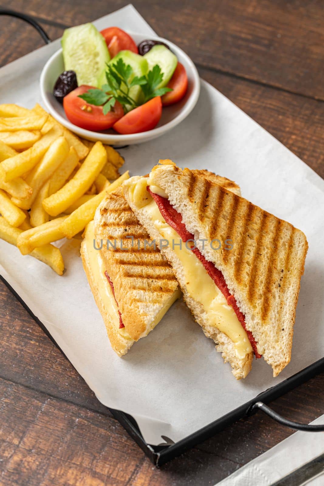 Toast with cheddar cheese and turkish sausage with french fries and salad on wooden table by Sonat