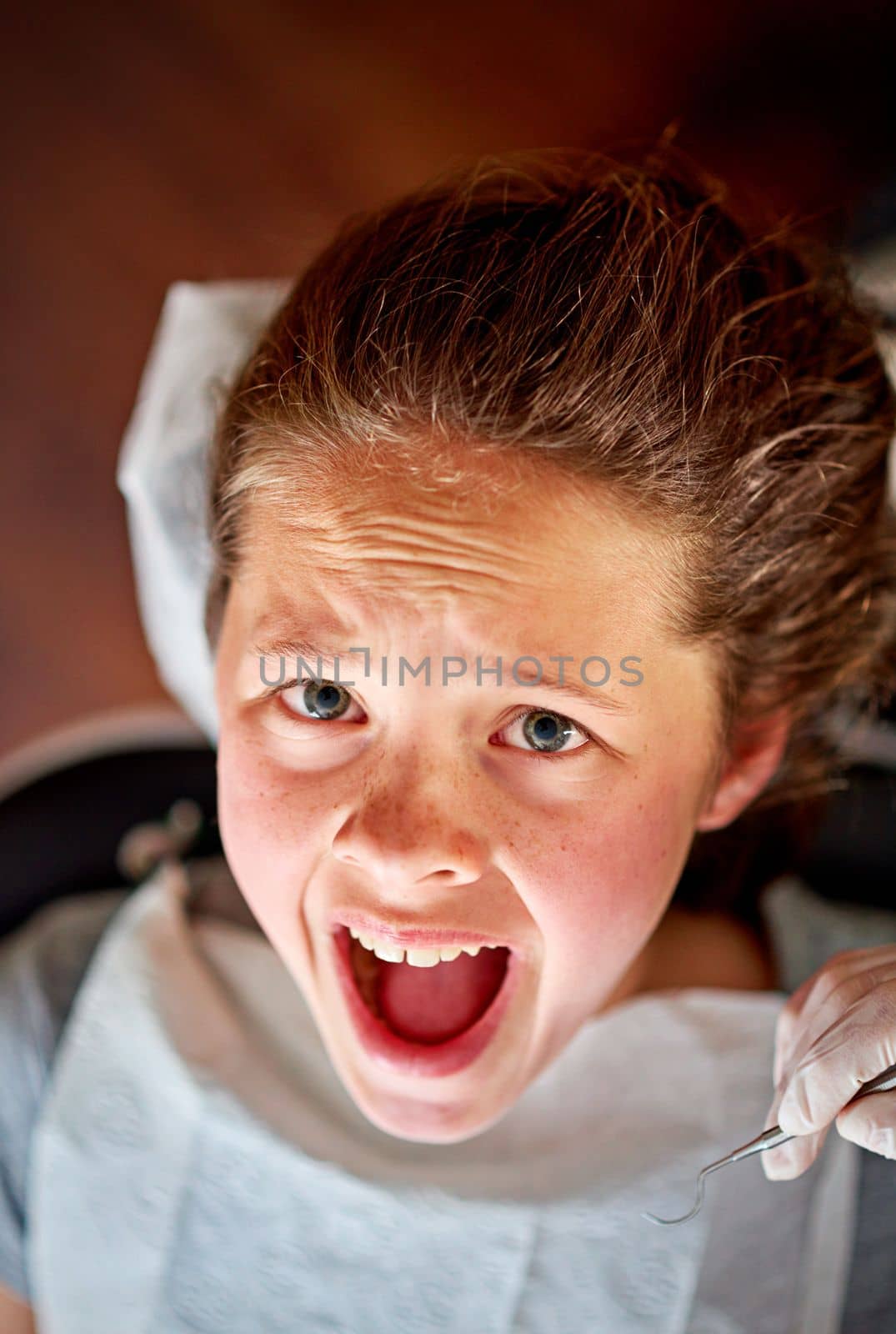 In the dreaded dentists chair. High angle shot of a young girl in the dentists chair looking terrified. by YuriArcurs