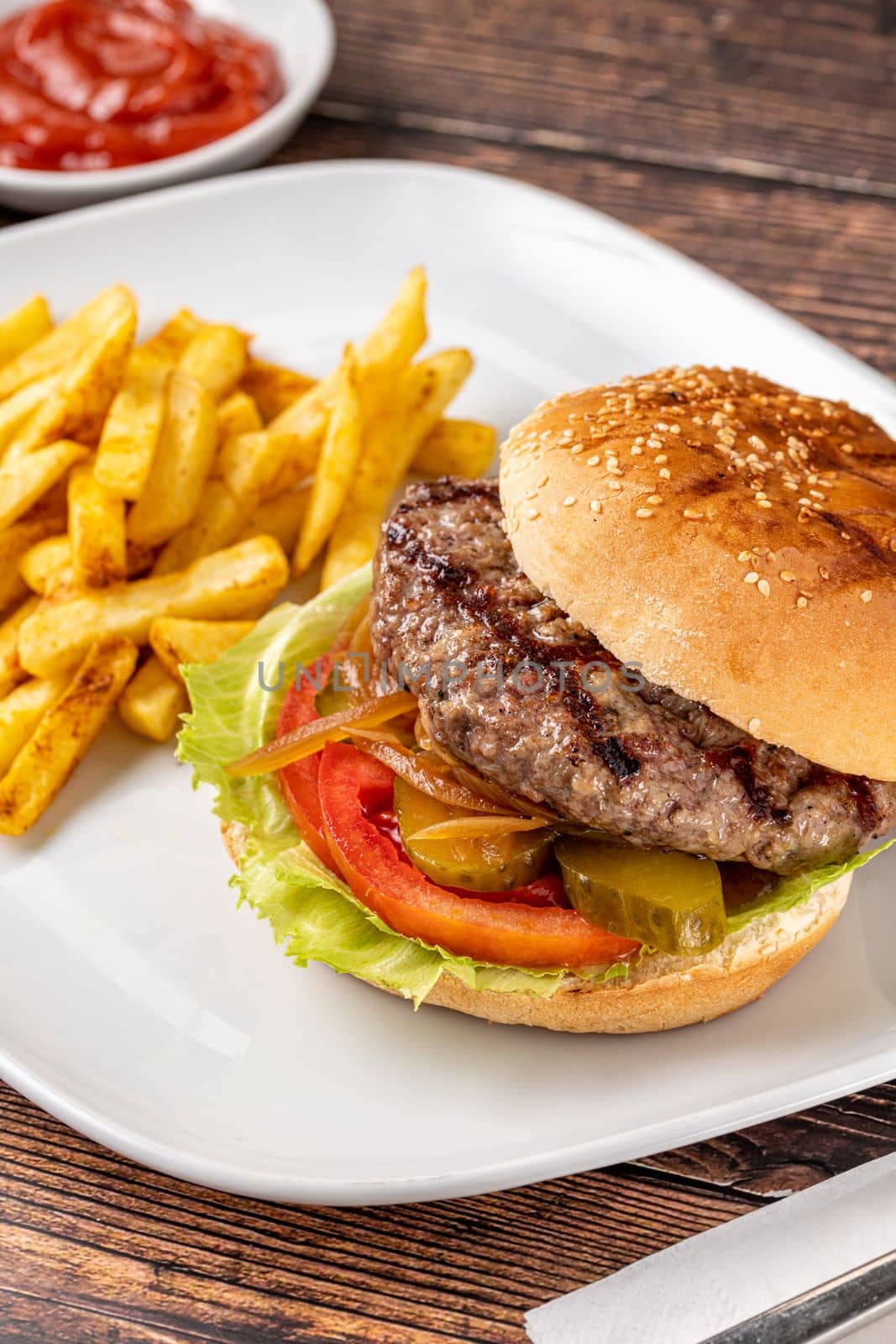 Delicious grilled homemade hamburger with beef, tomatoes, cheese, and lettuce on rustic wooden background by Sonat