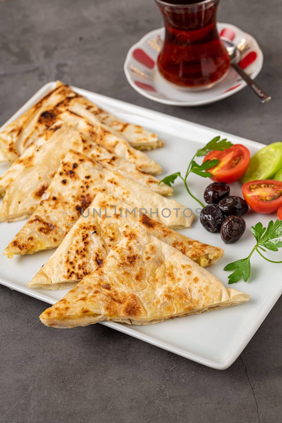 Traditional Turkish flatbread or Gozleme with tomatoes, olives and tea on dark stone table