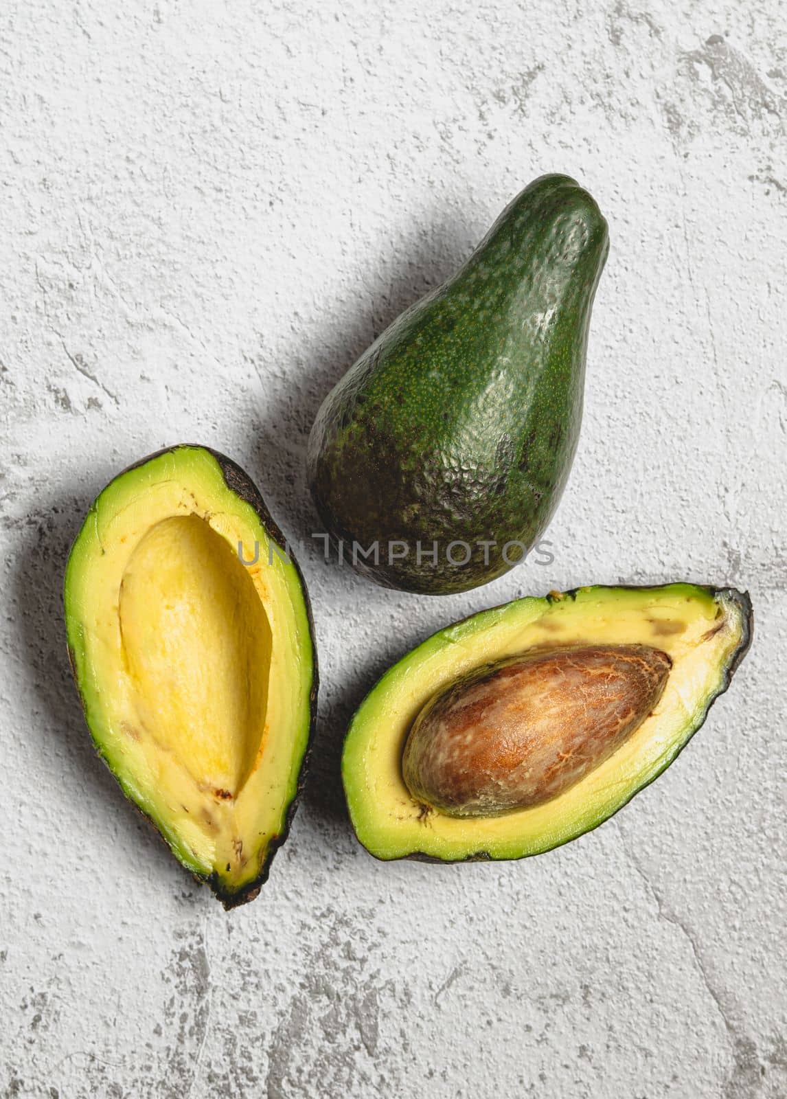 Top view of both cut and whole ripe avocado on white stone table