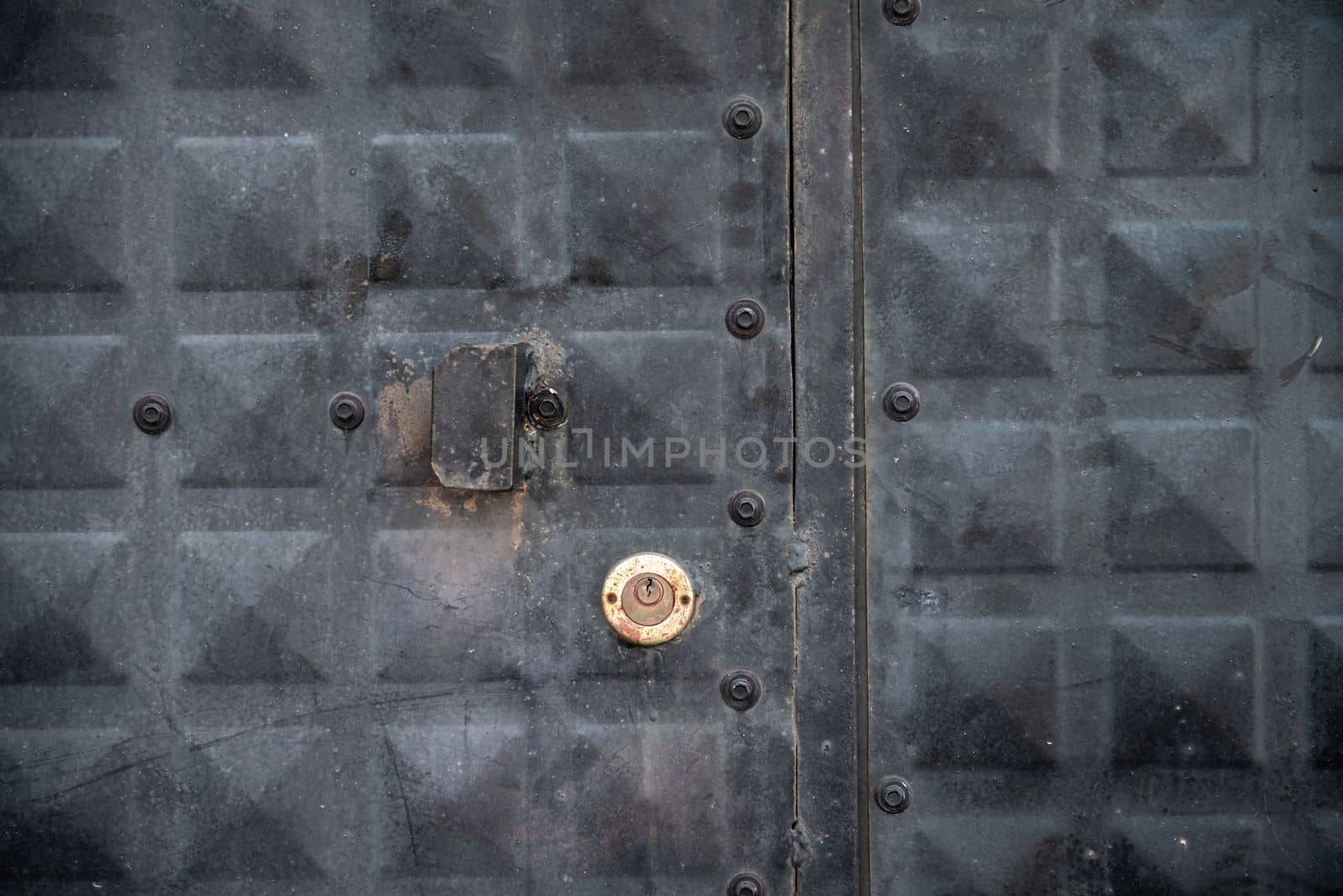 Front view of weathered black iron door with keyhole and lock