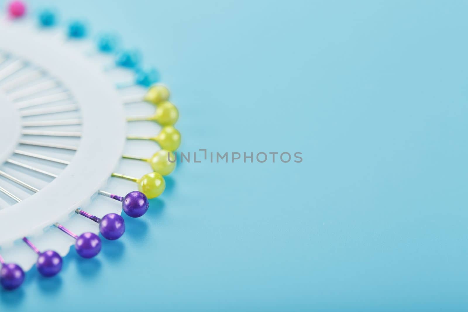 A set of multicolored needles pins in a round platform on a blue background with free space