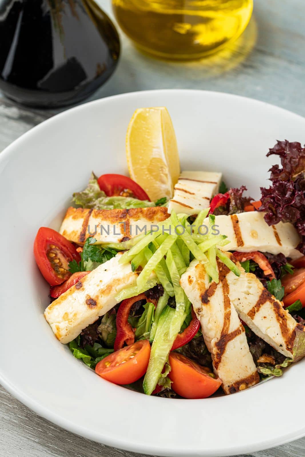 Salad with tomato and halloumi cheese on wooden table by Sonat