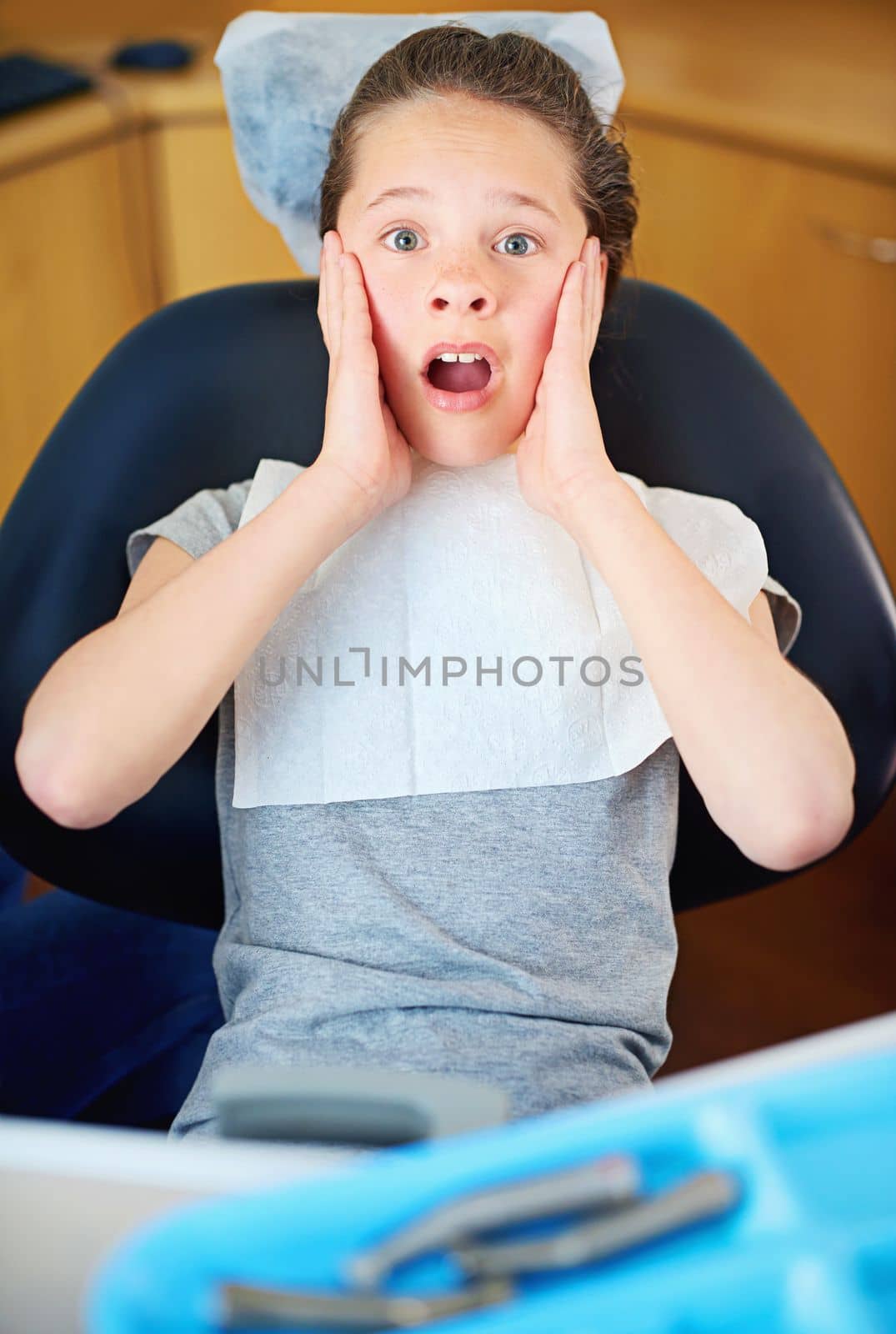 In the hot seat. a young girl looking terrified while sitting in a dentists chair