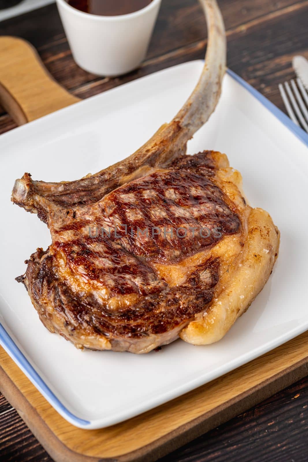 Grilled veal chop on white porcelain plate on wooden table