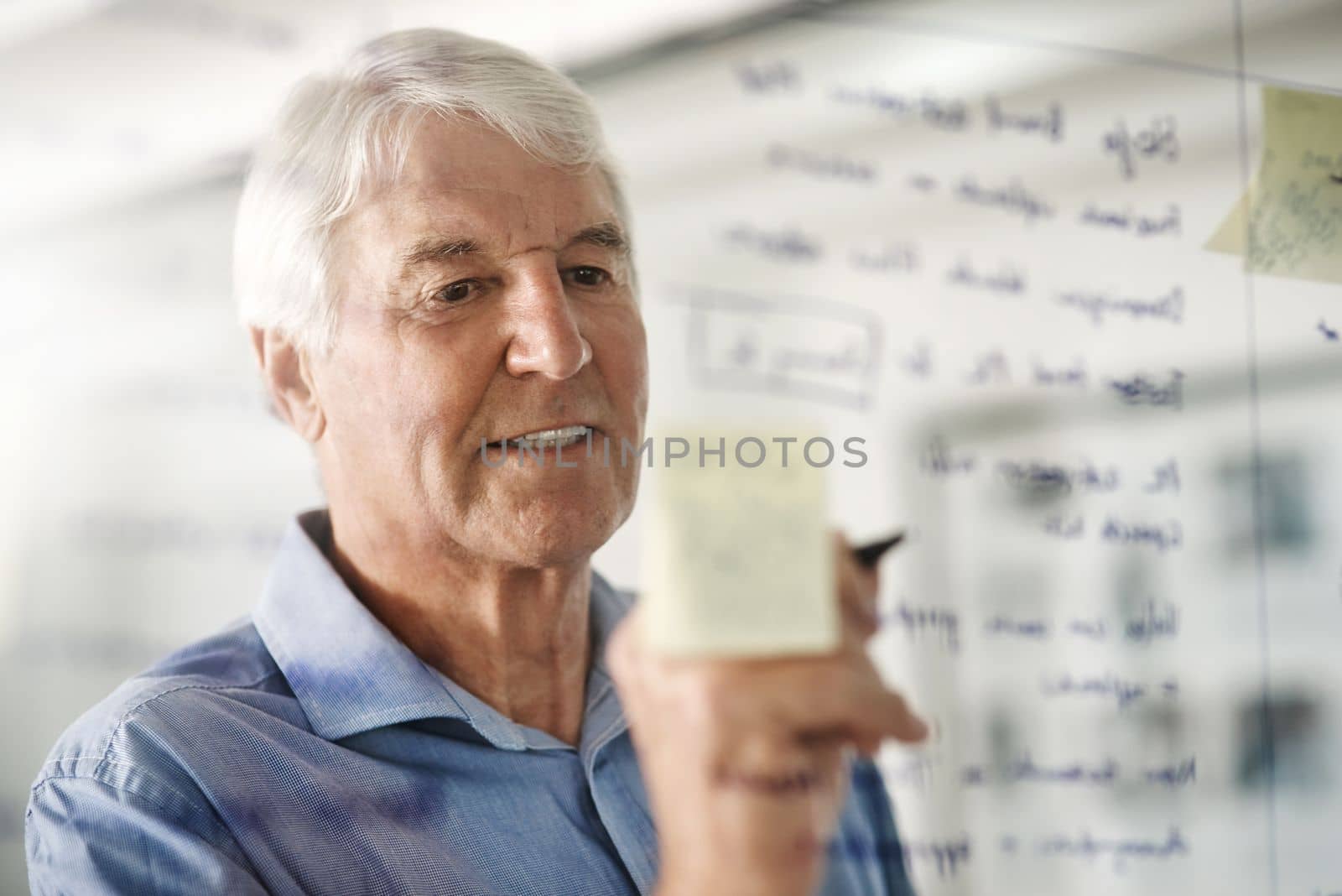 Owning a business is planning and execution. a senior businessman writing down ideas with a pen marker on a glass wall in the office
