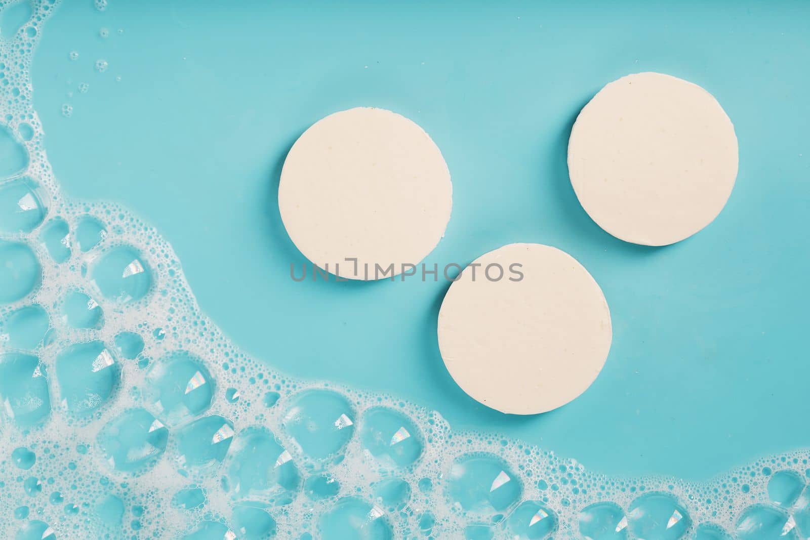 Three bars of round soap with foam on a blue background