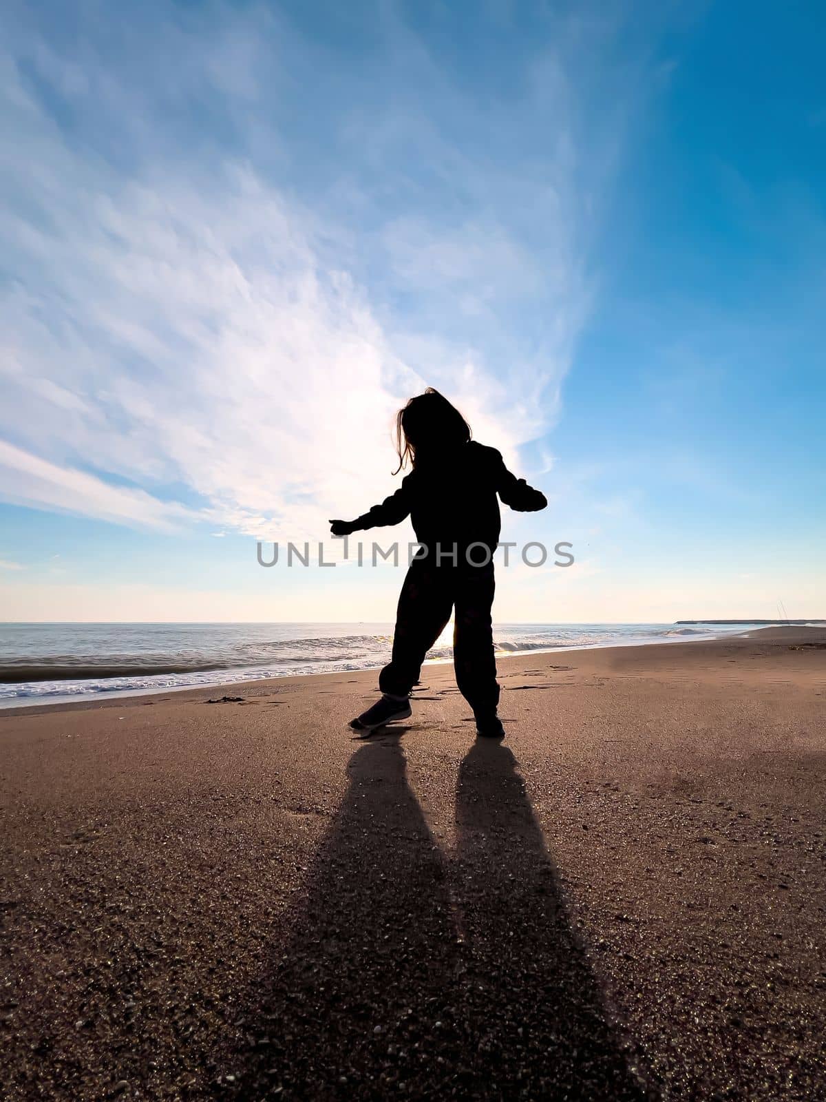 Silhouette of girl dancing on the beach at sunset in autumn by Sonat