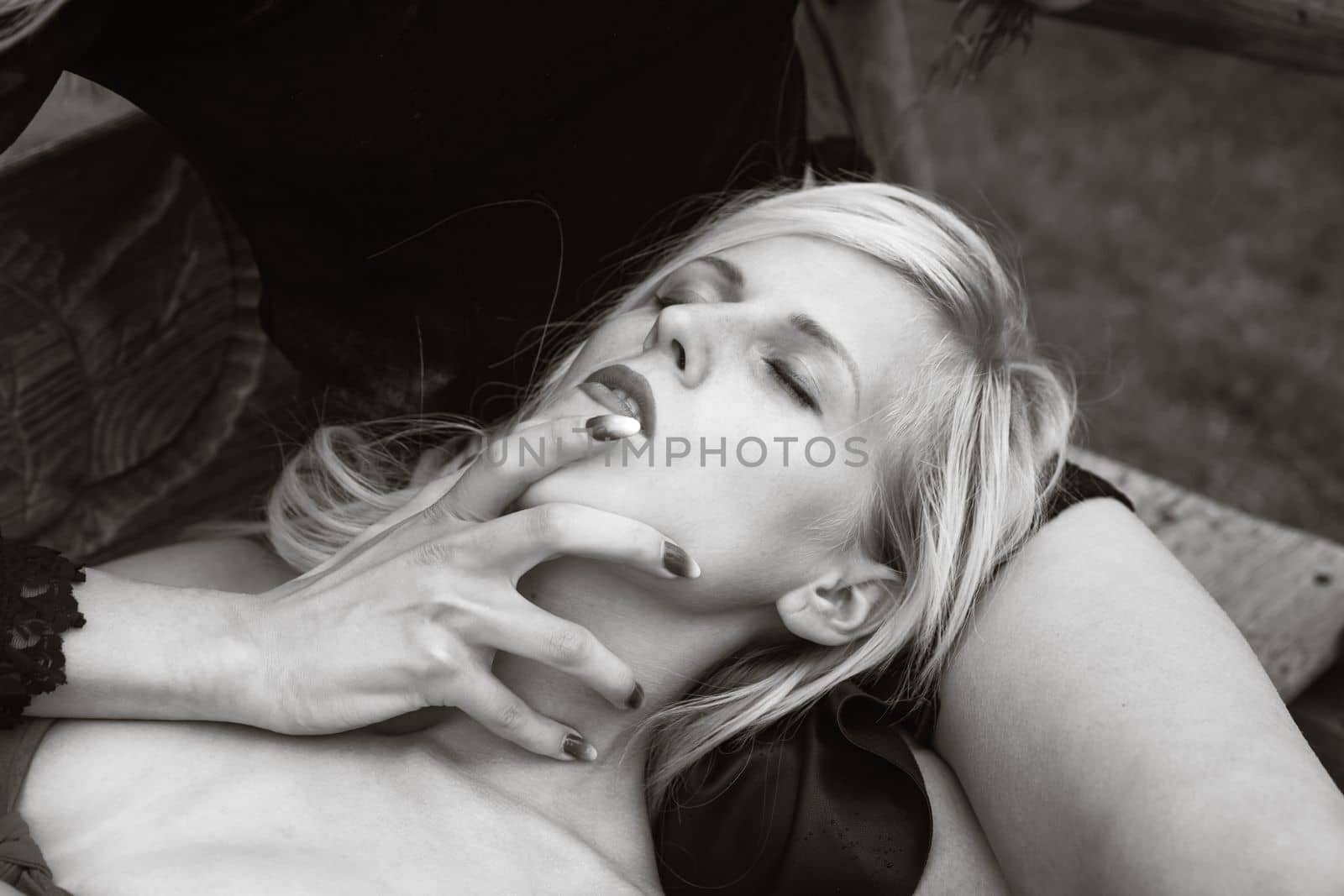 Romantic relationship. Two young women on outdoor wooden swings. A blonde girl in red is lying on the lap of a brunette girl in a black dress who has her hand on the blonde's throat