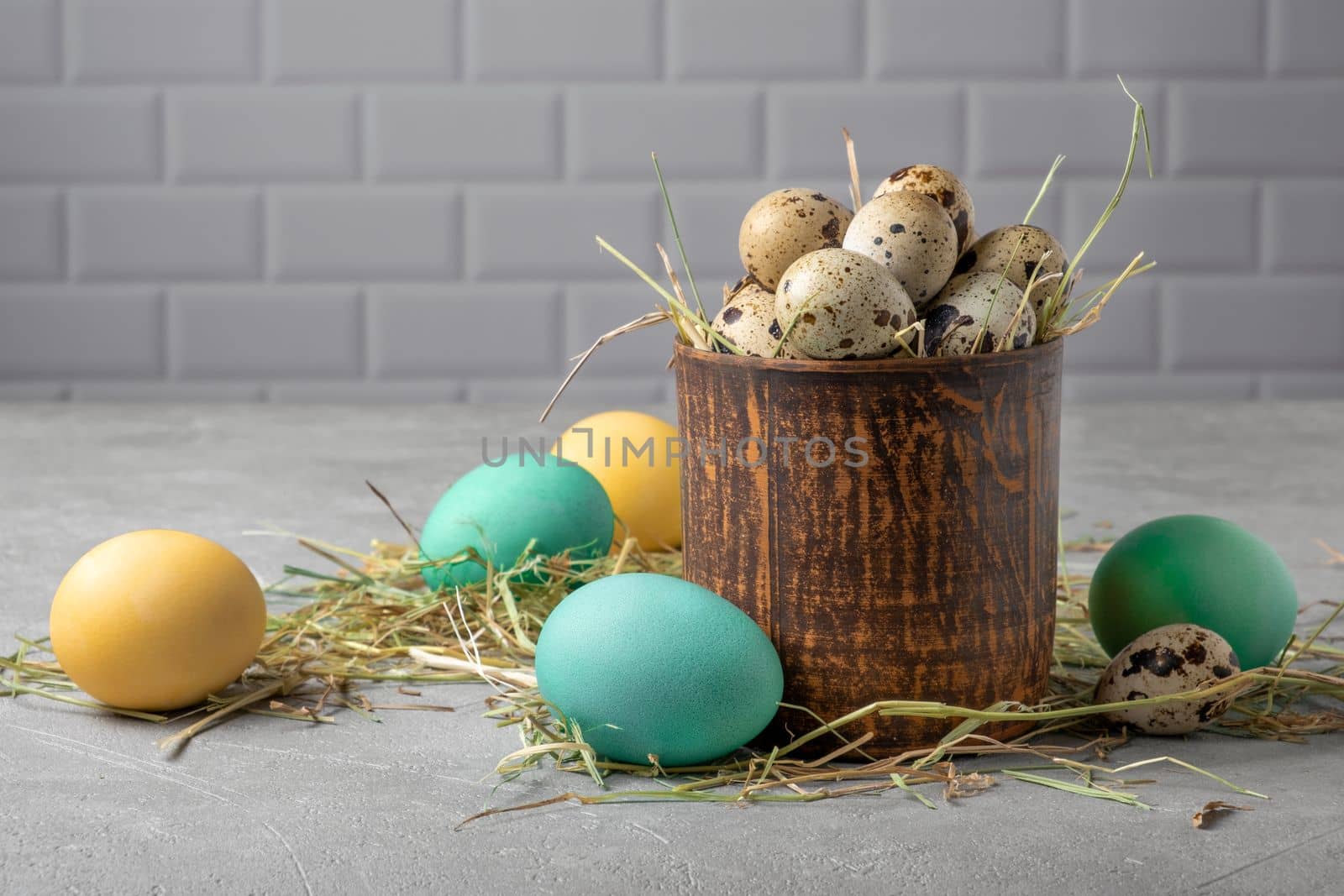 Easter composition from a clay vessel with quail eggs in hay surrounded by painted chicken eggs. Selective focus.