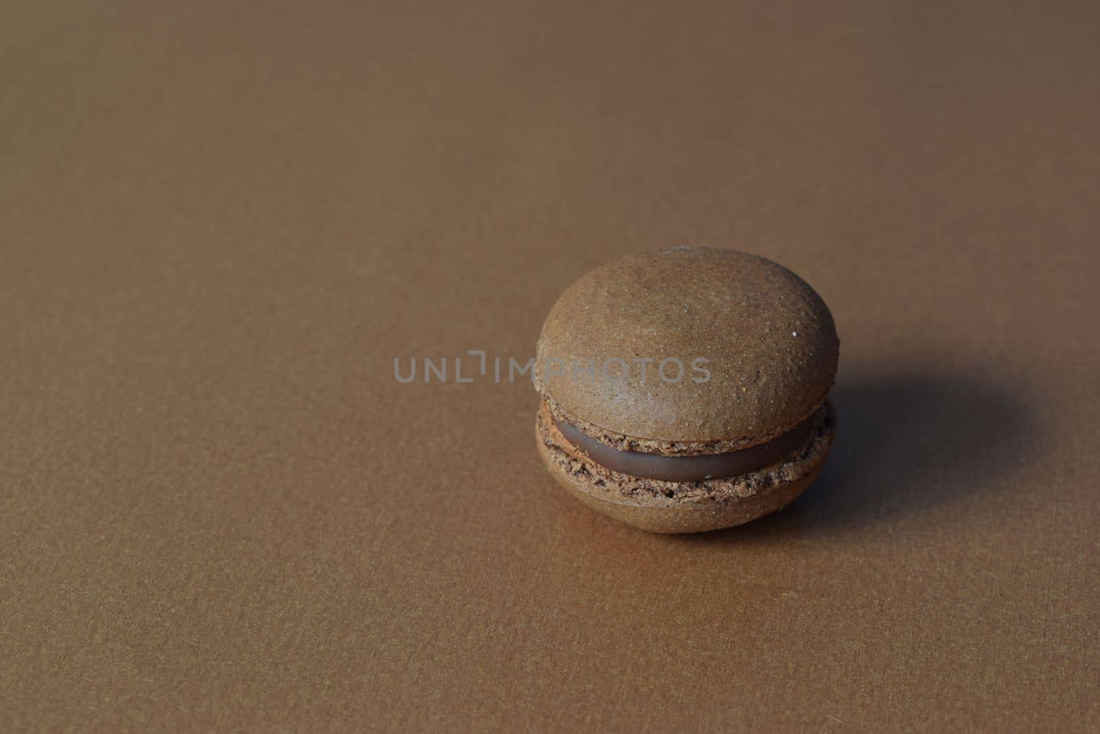 A brown macaron on a minimalistic brown background.