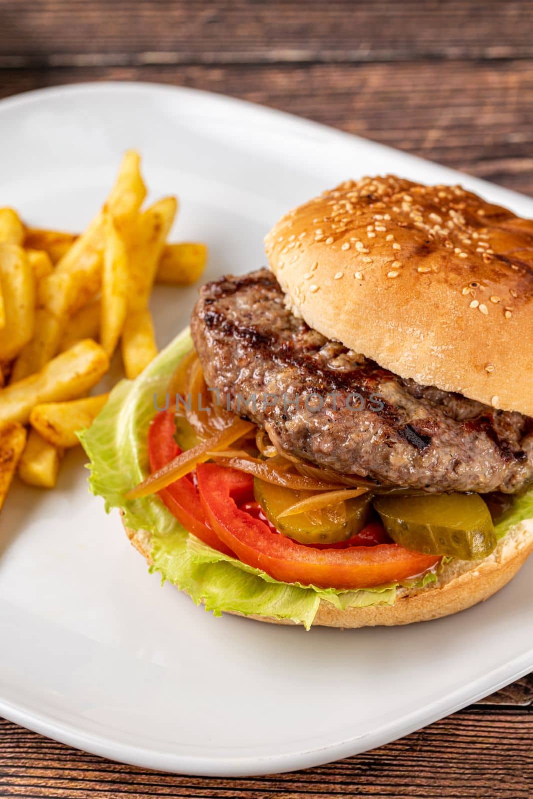 Delicious grilled burger on white plate on wooden table. With sauces and french fries