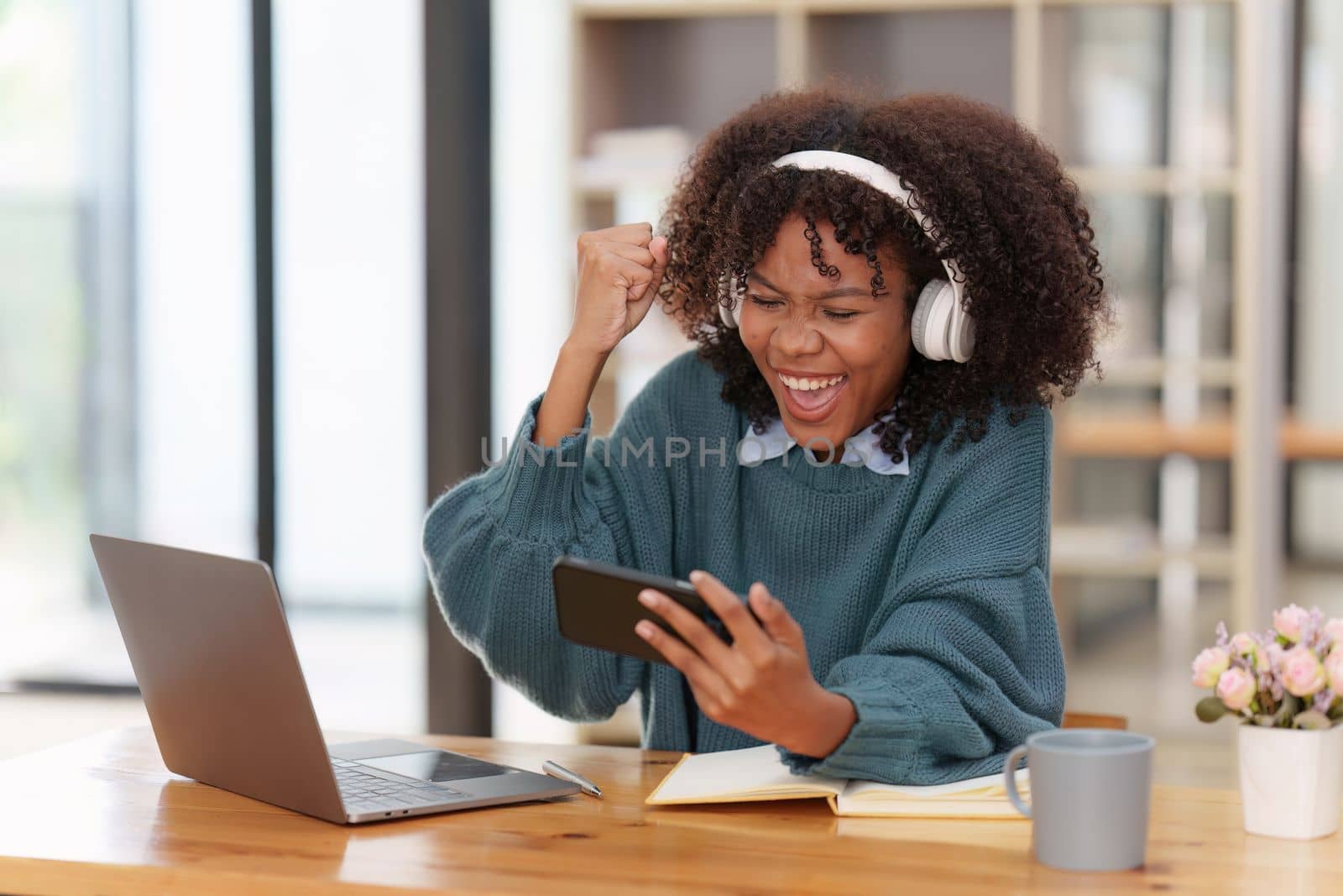 Excited Young black African woman wear headphone and enjoy with game via app on mobile phone