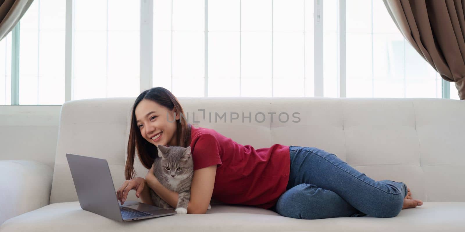 Attractive young woman on a laptop while sitting in a comfortable sofa at home with a funny assistant cat.