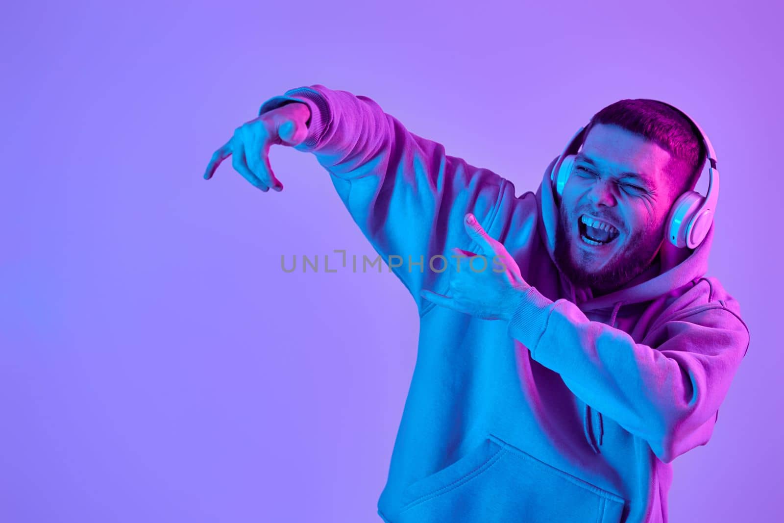 handsome bearded man with headphones in sweatshirt enjoying favorite music on purple neon background. Neon lighting